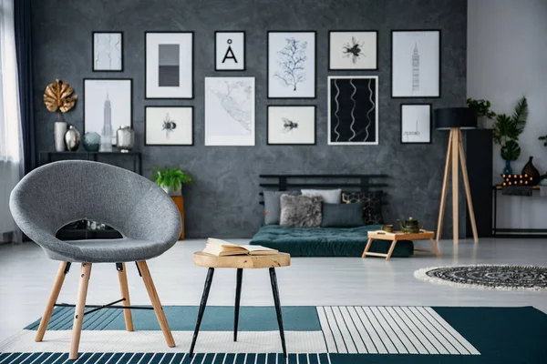 灰色扶手椅旁边的桌子上的地毯在客厅内与画廊的海报 背景模糊的真实照片 — 图库照片