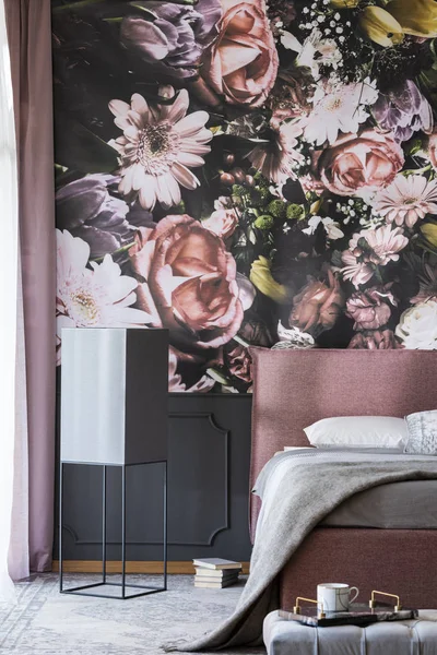 Flowers print on the wall in feminine bedroom interior with grey sheets on pink bed. Real photo