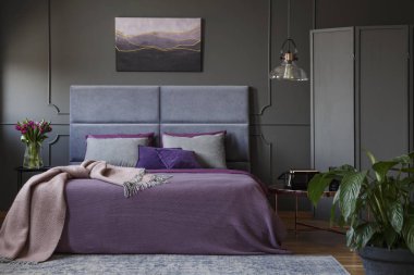 Real photo of stylish, artistic hotel interior with modern painting above violet bed with grey headboard clipart