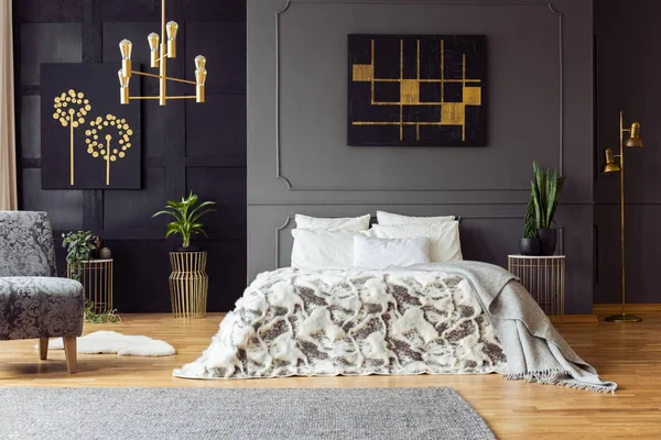 寝室のインテリア植物と肘掛け椅子でベッドの上の灰色の壁に黒とゴールドのポスター 実際の写真 — ストック写真