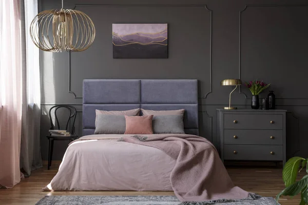 一个优雅的公寓内部为一个女人与灰色的抽屉柜站在粉红色的床旁边 — 图库照片