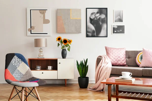 现代椅子和向日葵在内阁在平的内部与海报和粉红色枕头在沙发上 真实照片 — 图库照片