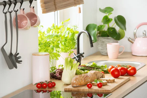 新鲜蔬菜和面包放在台面上的真实照片厨房内饰与粉彩粉红色水壶和杯子 — 图库照片