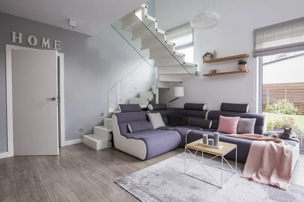 Corner sofa with pink blanket next to stairs in apartment interior with door and table. Real photo