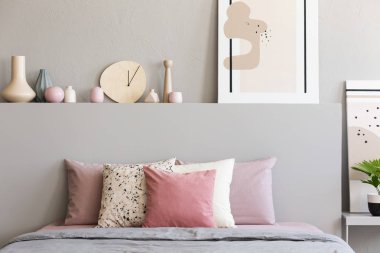 Yatak başı üzerinde posteri ile pembe ve beyaz yastıklar pastel yatak odası iç gri yatakta. Gerçek fotoğraf