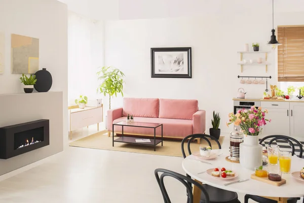暖炉の近くのピンクの長いすの上のポスターと白いアパート インテリアでテーブルに花 実際の写真 — ストック写真