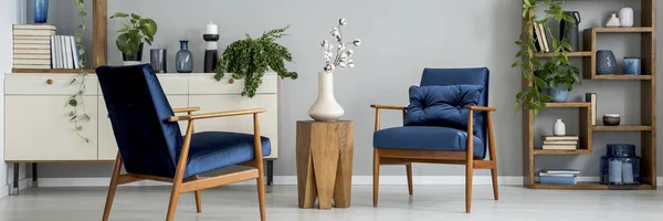 皇家蓝色扶手椅 带坐垫 在明亮的起居室内有新鲜的植物 鲜花在餐桌上和货架上的书籍和装饰 — 图库照片