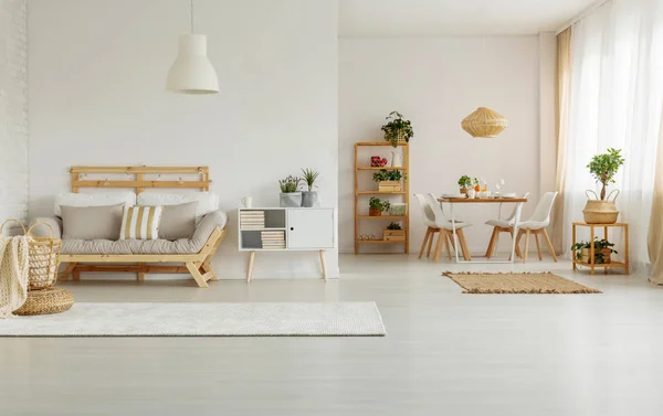 Wooden sofa next to white cabinet in minimal apartment interior with plants and lamps. Real photo
