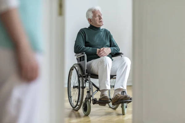 在医院里坐轮椅的可怜的残疾老人 前景模糊的护士 — 图库照片