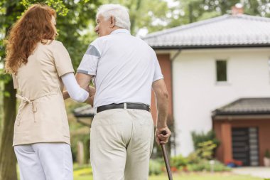 Bir baston ve bakım evine yürürken Bahçe dışında onun caregiver arkasında yaşlı bir adam.