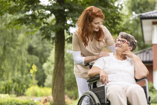 一位女志愿者帮助一位在退休家庭花园里坐轮椅的老年妇女 — 图库照片
