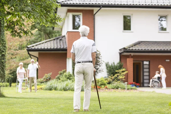 高級老人ホームの外の彼の仲間の仲間を見て杖を持った白髪の年配の男性バック — ストック写真