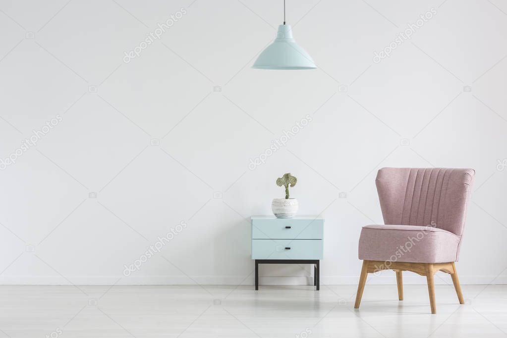 Pink chair next to cabinet with plant in apartment interior with lamp and copy space. Real photo with a place for your poster