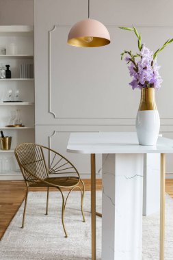 Altın sandalyenin altına gri yemek odası iç pembe lamba yakınındaki beyaz mermer masaya çiçek. Gerçek fotoğraf