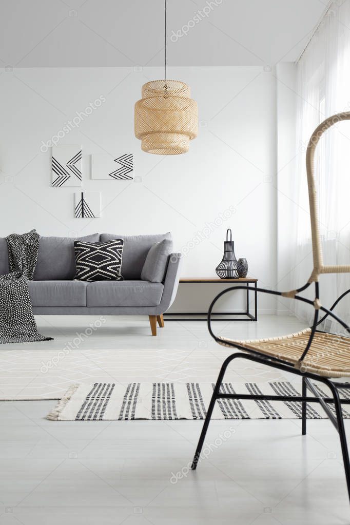 Lamp in white spacious apartment interior with patterned blanket on grey couch. Real photo