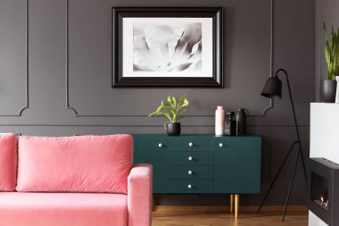 Karanlık oturma odası iç tesisi ve vazolar, metal lamba ve toz pembe kanepe gerçek fotoğraf ile yeşil dolap ile kalıplama ile duvarda asılı siyah ve beyaz poster