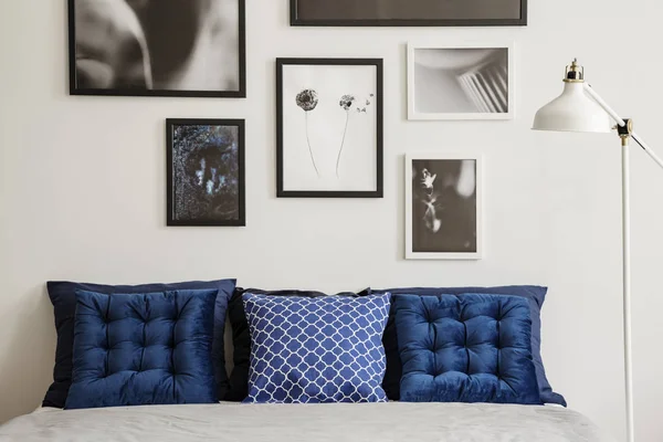 海军蓝色垫子在床旁边的灯在白色卧室内部与画廊的海报 真实照片 — 图库照片