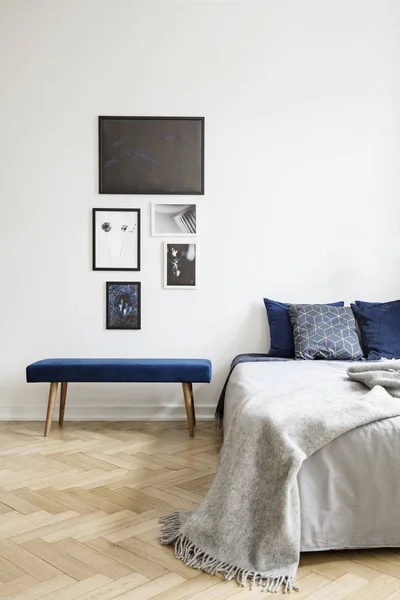 海报上面的蓝色长凳旁边的床与灰色毯子在白色简单的卧室内部 真实照片 — 图库照片