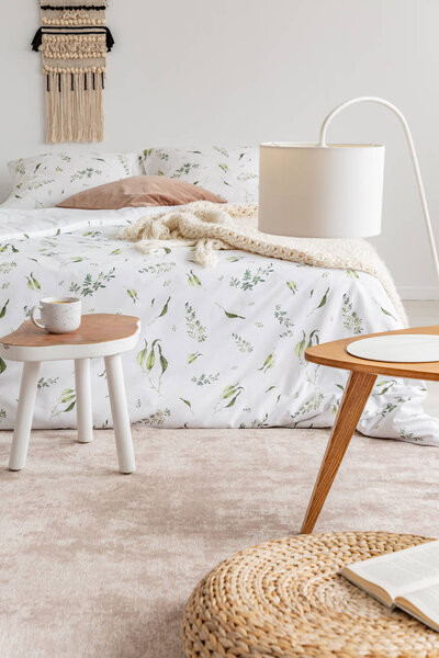 A cozy pastel bedroom interior with a bed dressed in green plants on white linen and cushions. Soft peach color rug on the floor. Real photo.