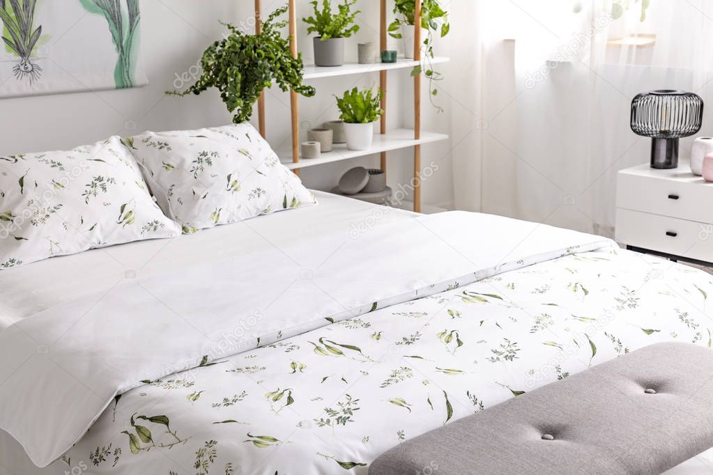 Close-up of a bed dressed in organic cotton green plants pattern white linen in a sunny bedroom interior. Real photo.