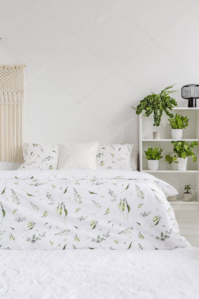 Scandinavian style bedroom interior with green plants pattern on white bedding lying on a bed. Fluffy rug on the floor. Empty wall in the background. Real photo.