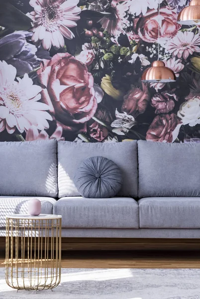 Round pillow on a sofa and floral wallpaper in a living room interior. Real photo