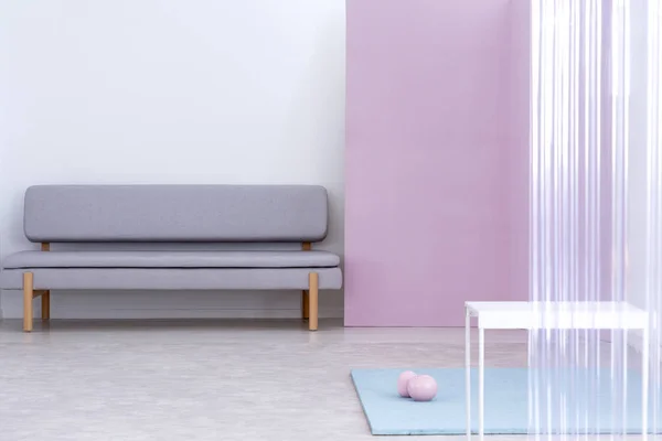 Real photo of a gray sofa standing in a simple living room interior with pink wall and white, metal table