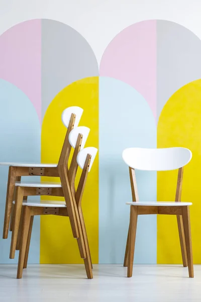 Classic, wooden dining chairs with white elements in front of geometric decorations in a colorful room interior. Real photo.