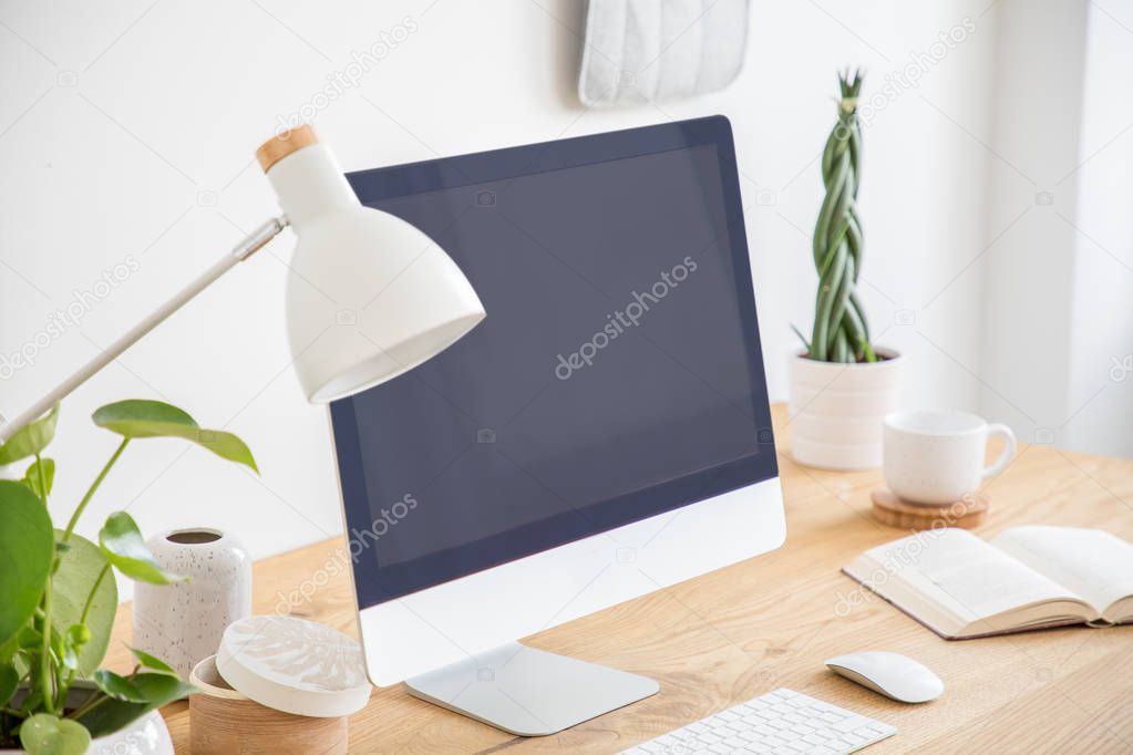 White lamp next to black desktop computer on wooden desk in freelancer's interior. Real photo