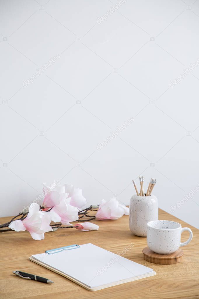 Sheets of paper, pen, mug and flowers on a table. Empty wall above, place your poster