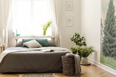 Doğa yatak odası iç ahşap zemin üzerinde bir yatak, duvar ve parlak bir pencere içinde belgili tanımlık geçmiş bir yaprak dökmeyen ağaç poster ile toprak renklerde. Gerçek fotoğraf.