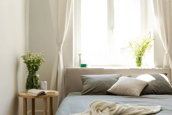 阳光明媚的早晨 在自然风格的卧室里有一张床 一张床头柜和一束野花 大明亮的窗口在背景 真实照片 — 图库照片