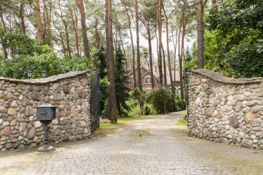 Entrance gate to a rustic, english house in the forest with stone wall and cobblestone driveway clipart