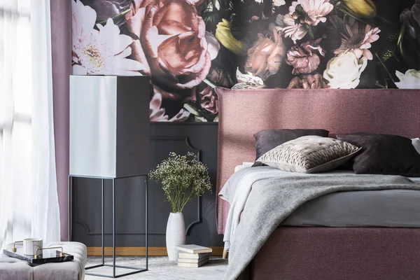 花と模様の寝室のインテリアで灰色の枕とピンクのベッドの横に本 実際の写真 — ストック写真