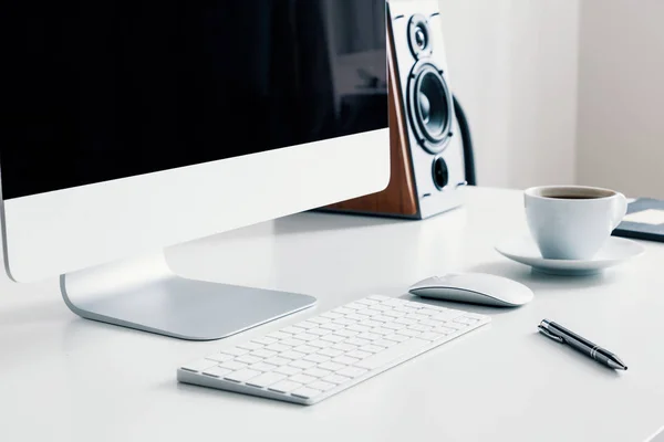 Cup of coffee, keyboard and desktop computer on desk in white home office interior. Real photo