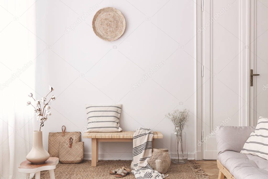 Flowers on wooden table near bench with pillow and blanket in white living room interior. Real photo