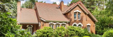 Kırmızı tuğla İngiliz tarzı klasik ev dik bir çatı ve büyük pencereler ağaçlar ve yeşil bitkiler ile çevrilidir. Panorama.