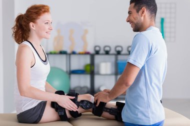 Profesyonel fizyoterapist kadın bacak yaralanma ile yardım gülümseyen 