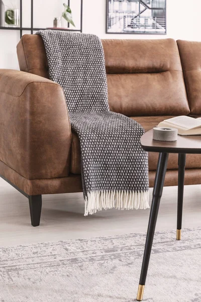 Close-up on blanket on leather couch near table in modern living room interior. Real photo