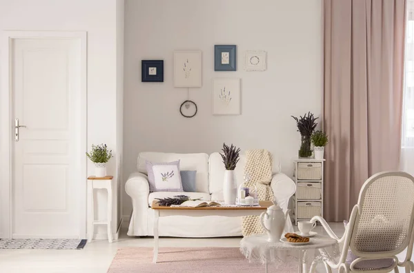 在粉红色起居室的白色沙发前 桌子上摆着一张鲜花 里面有门和扶手椅 真实照片 — 图库照片