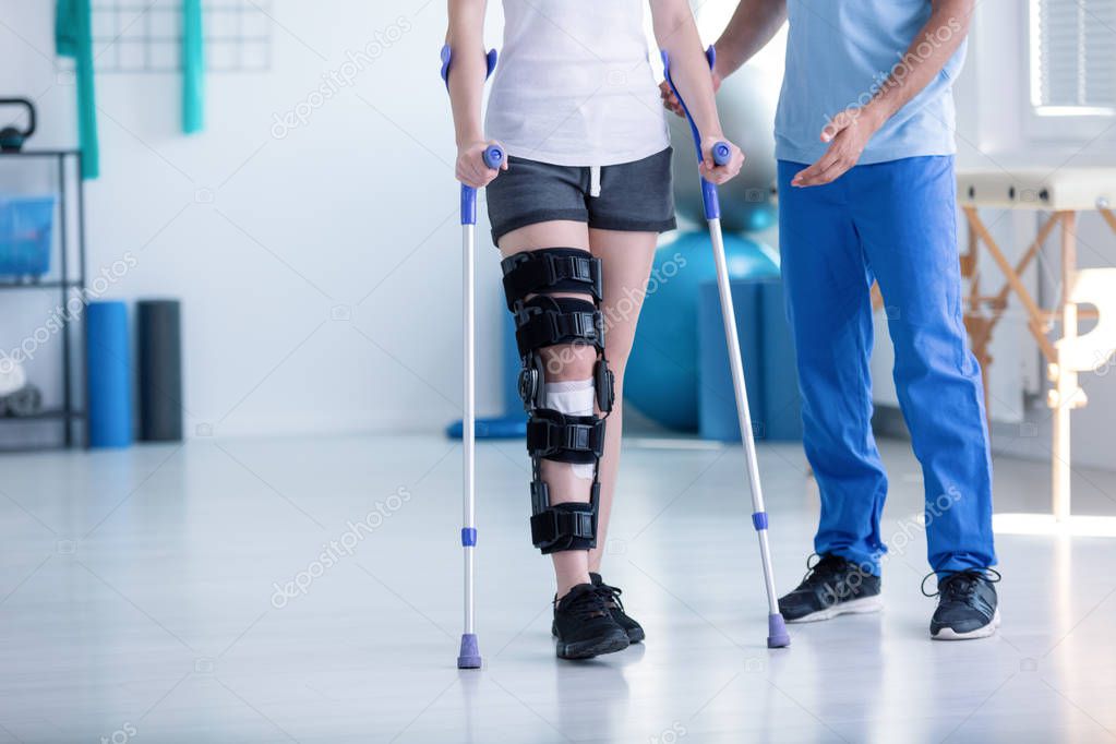 Sport physiotherapist and patient with leg injury during training with crutches