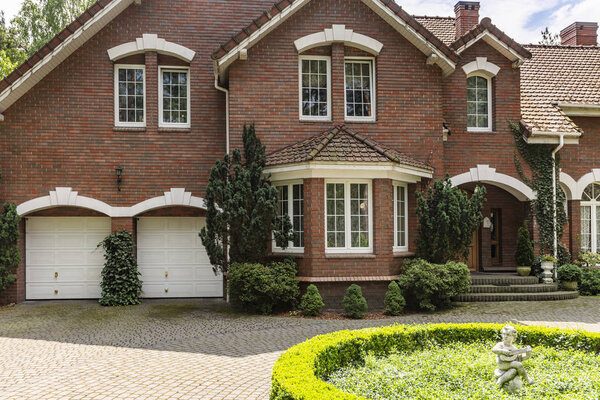 Real photo of a brick house with a bay window, garages and round garden in front of the entrance