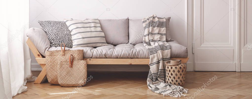 Panorama of pillows and blanket on wooden beige couch in white flat interior with door. Real photo