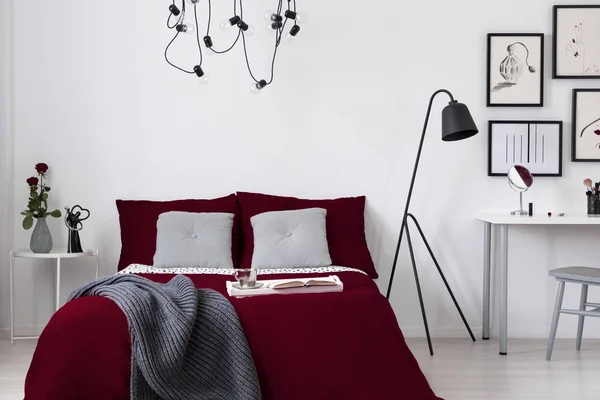 A burgundy bedding and gray pillows on a bed in a white wall bedroom interior. Real photo.