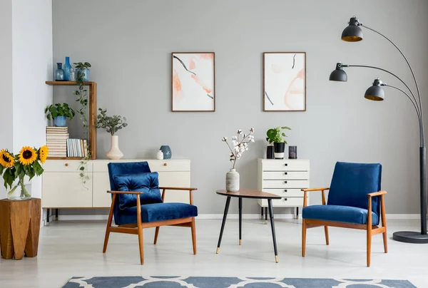 木桌与鲜花之间的蓝色扶手椅在灰色扁平内饰与海报 真实照片 — 图库照片