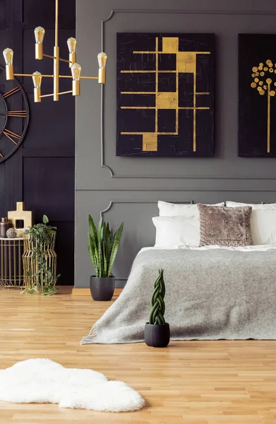 金色和黑色的画挂在床上与明亮的床单在真实照片的深色卧室内饰与新鲜的植物和墙上的造型 — 图库照片