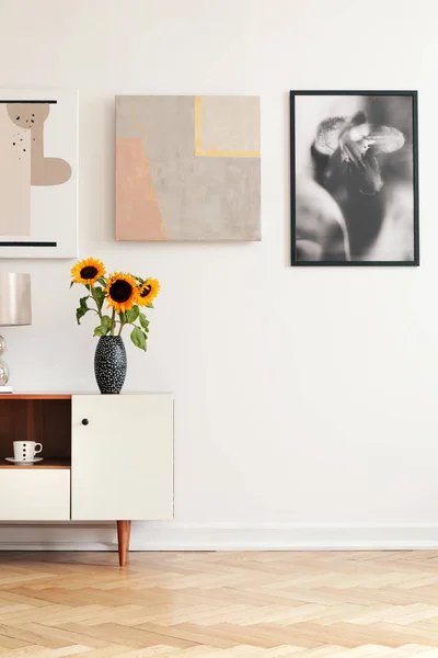 真正的照片与空的空间为您的扶手椅在白色客厅内部与新鲜的向日葵在橱柜 人字形实木复合地板和海报墙上 — 图库照片