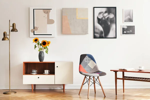 Real photo of bright eclectic living room interior with many posters, colorful chair, wooden cupboard with flowers and coffee table with book and cup — Stock Image Real Photo Bright Eclectic Living Room Interior Many Posters Colorful Stock Photo