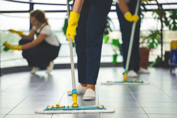 用黄色手套和拖把擦拭地板的专业清洁剂特写 — 图库照片