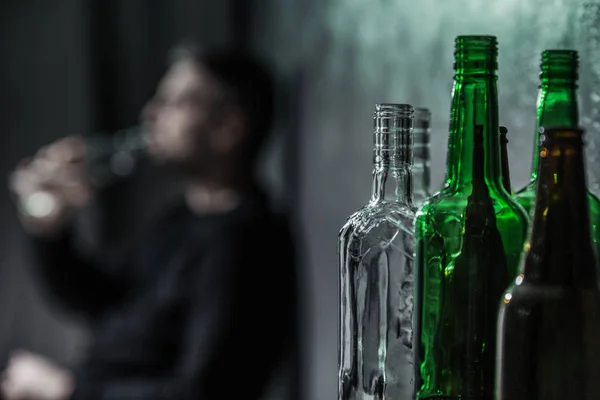Γκρο Πλαν Μπουκάλια Και Θολή Άτομο Κατανάλωση Αλκοόλ Στο Παρασκήνιο — Φωτογραφία Αρχείου